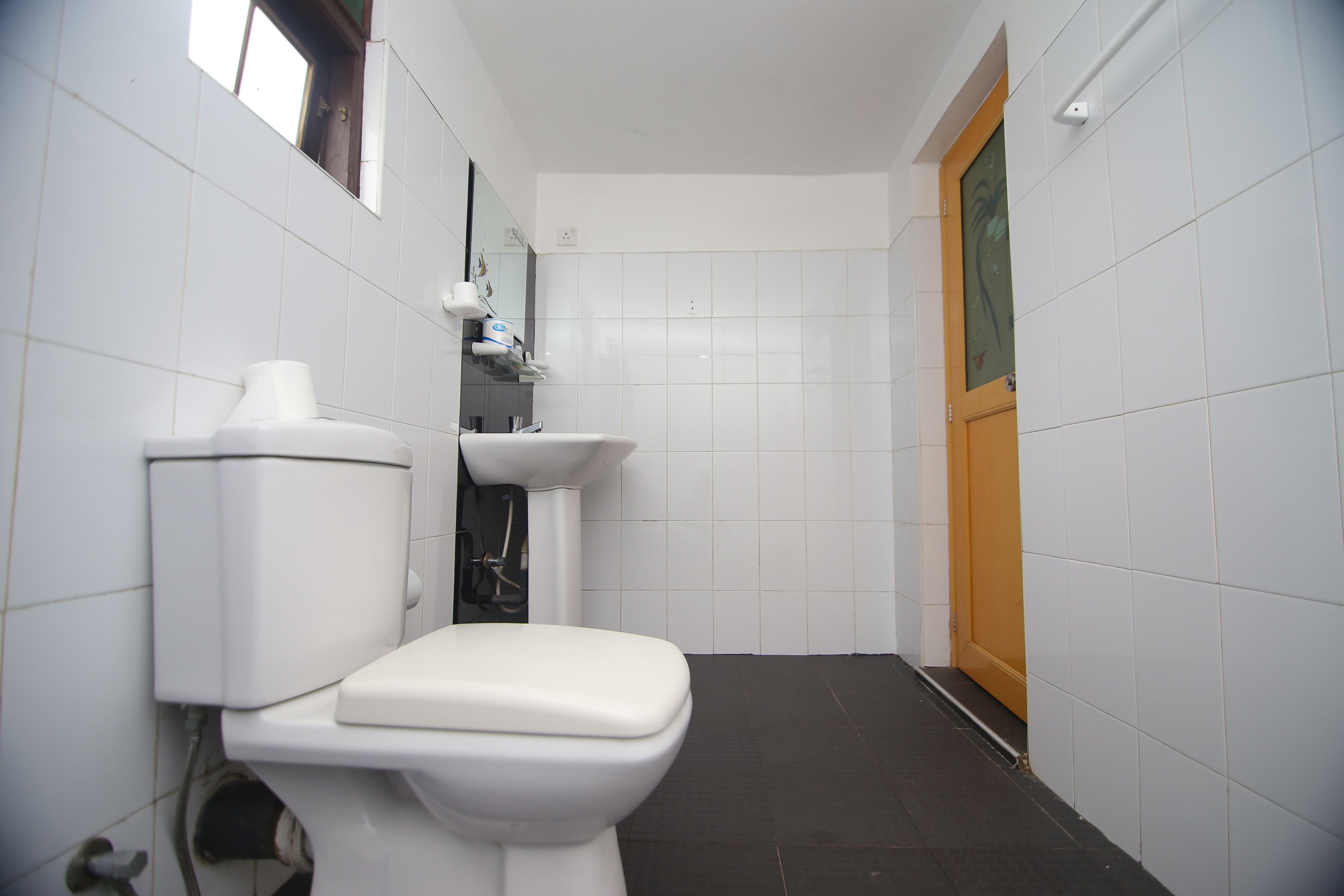 A small, clean bathroom with white tiles, a toilet, a sink, and a mirror.