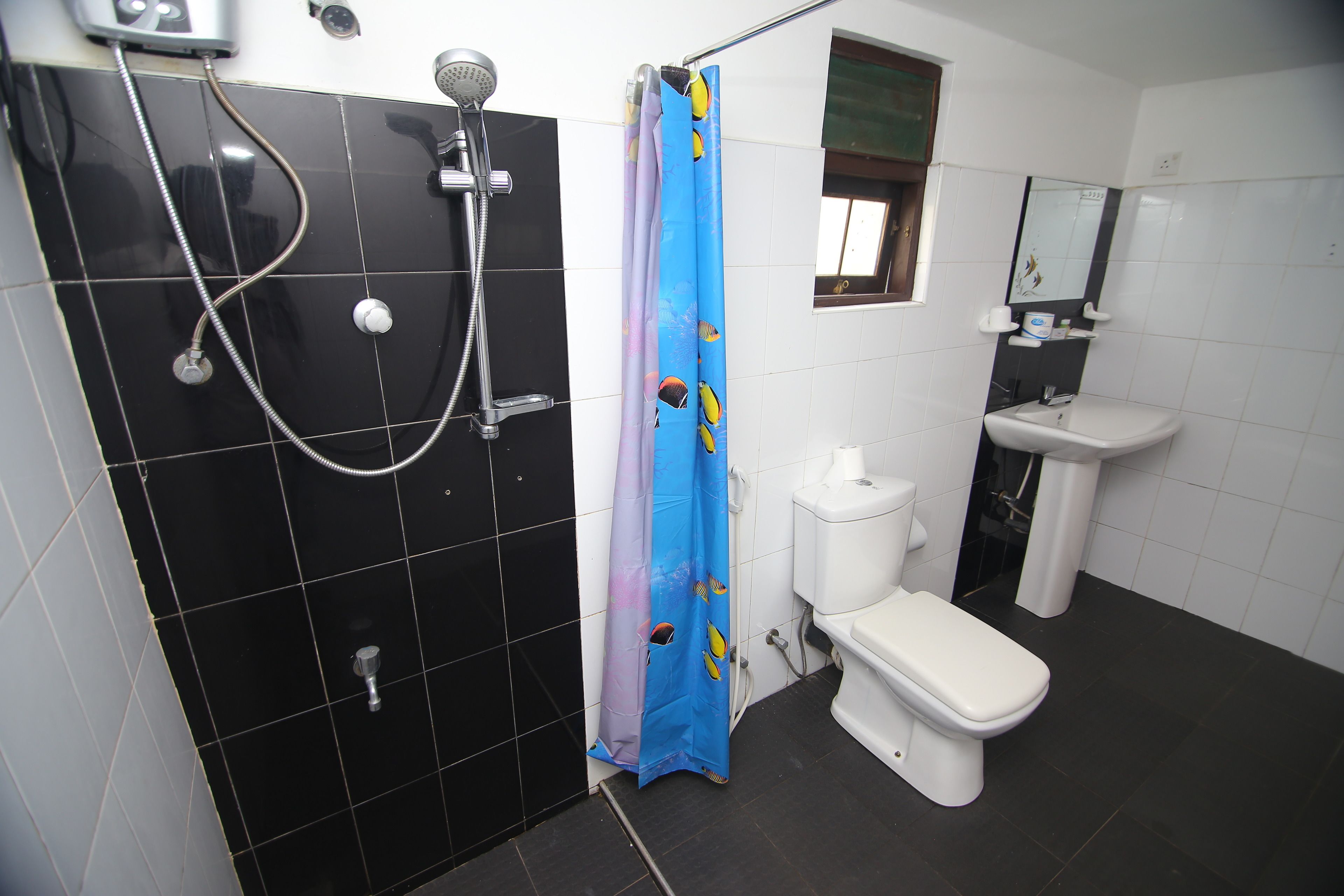 A bathroom with a black tiled wall, a shower, a toilet, and a sink.
