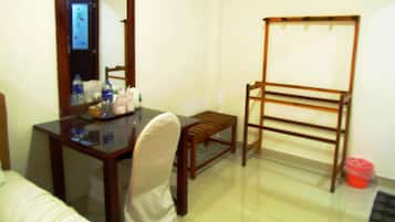 Una habitación pequeña con un escritorio de madera, una silla, un espejo, un perchero de madera y un bote de basura rojo.