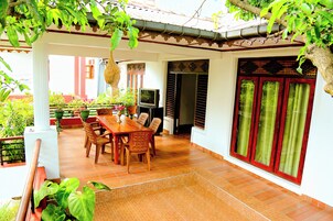 Un patio cubierto con una mesa y sillas de madera, un televisor y una puerta tradicional con detalles rojos.