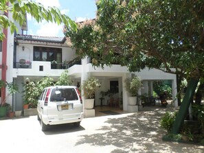 A white van parked in front of a two-story building with balconies and potted plants. - Thilaka City Hotel (Anuradhapura)