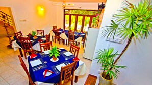 Un comedor con mantel azul, sillas de madera y plantas en macetas.