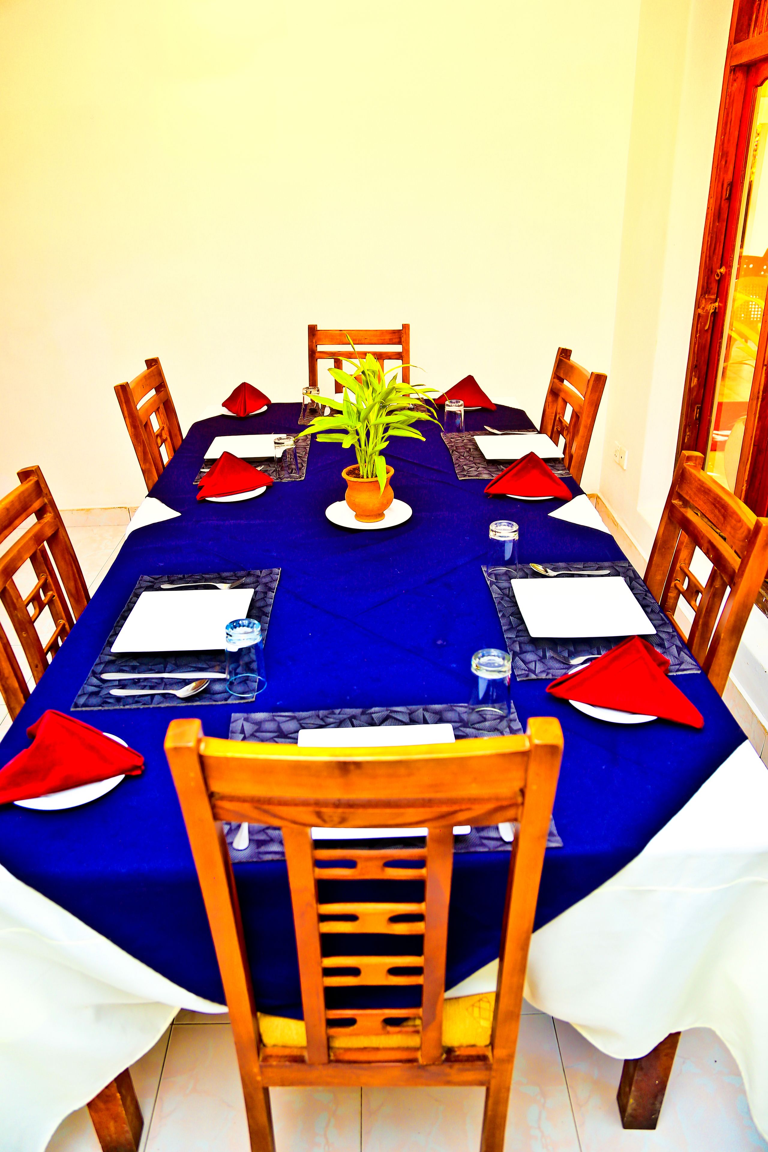 Une table à manger dressée pour six personnes, avec une nappe bleue, des chaises en bois et des serviettes rouges.