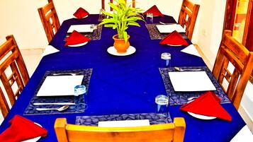 Mesa de jantar posta para seis pessoas, com toalha azul, cadeiras de madeira e guardanapos vermelhos.