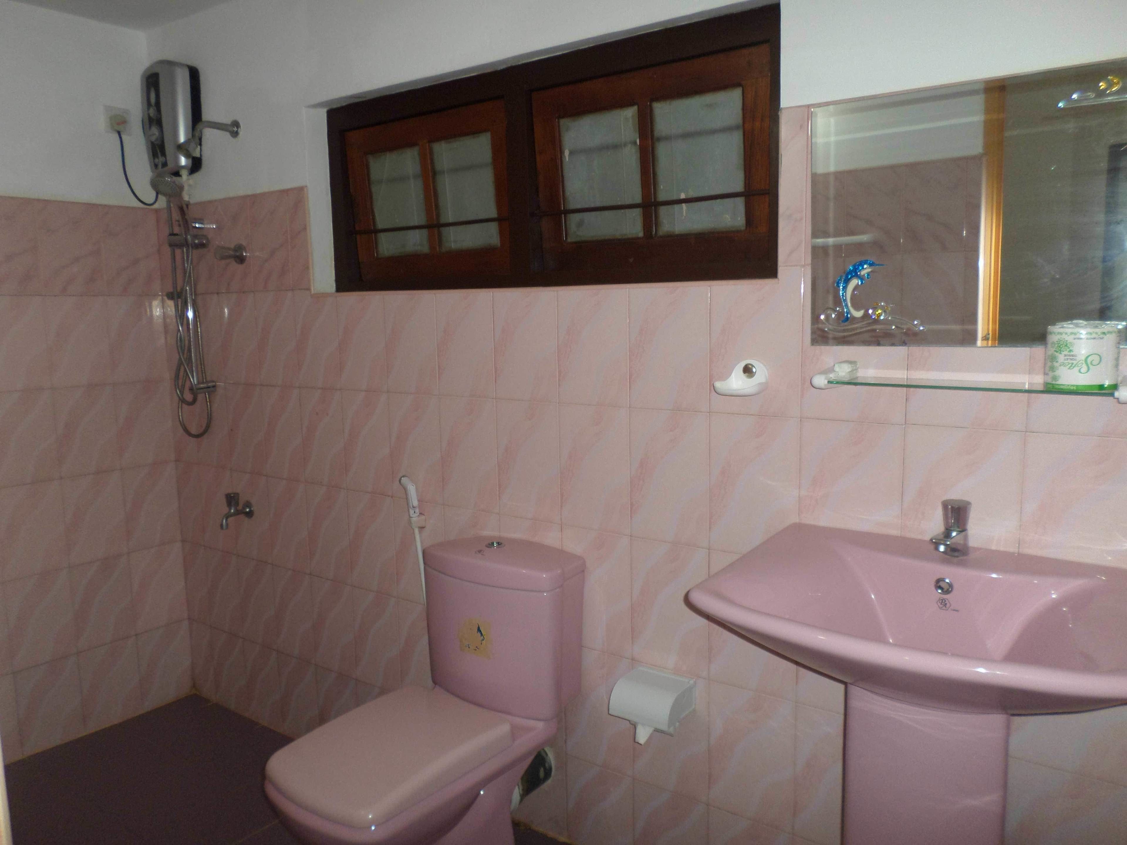 Un baño con inodoro rosa, lavamanos y ducha.