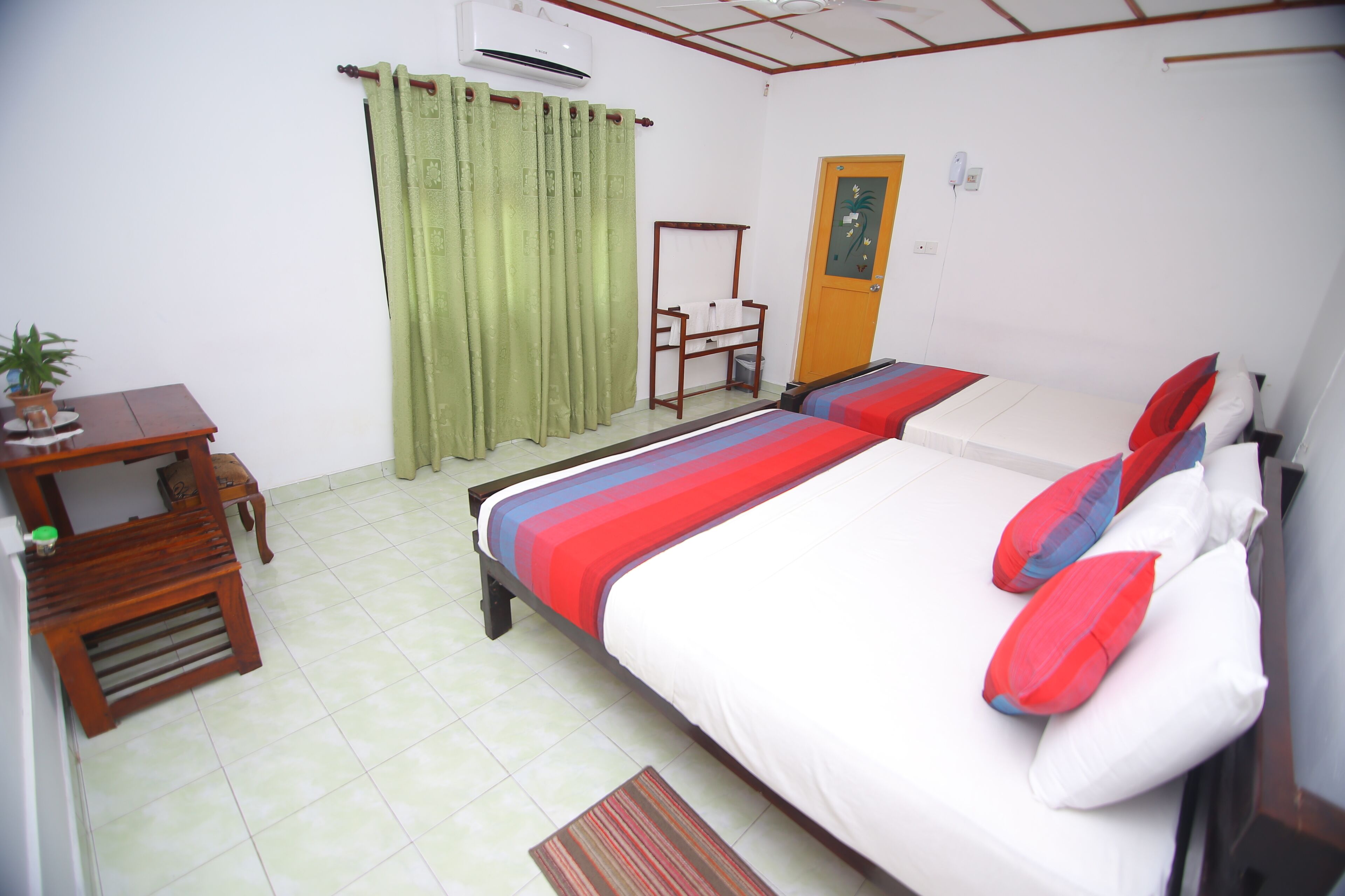 A bedroom with a bed, a desk, a chair, a door, and a curtain.