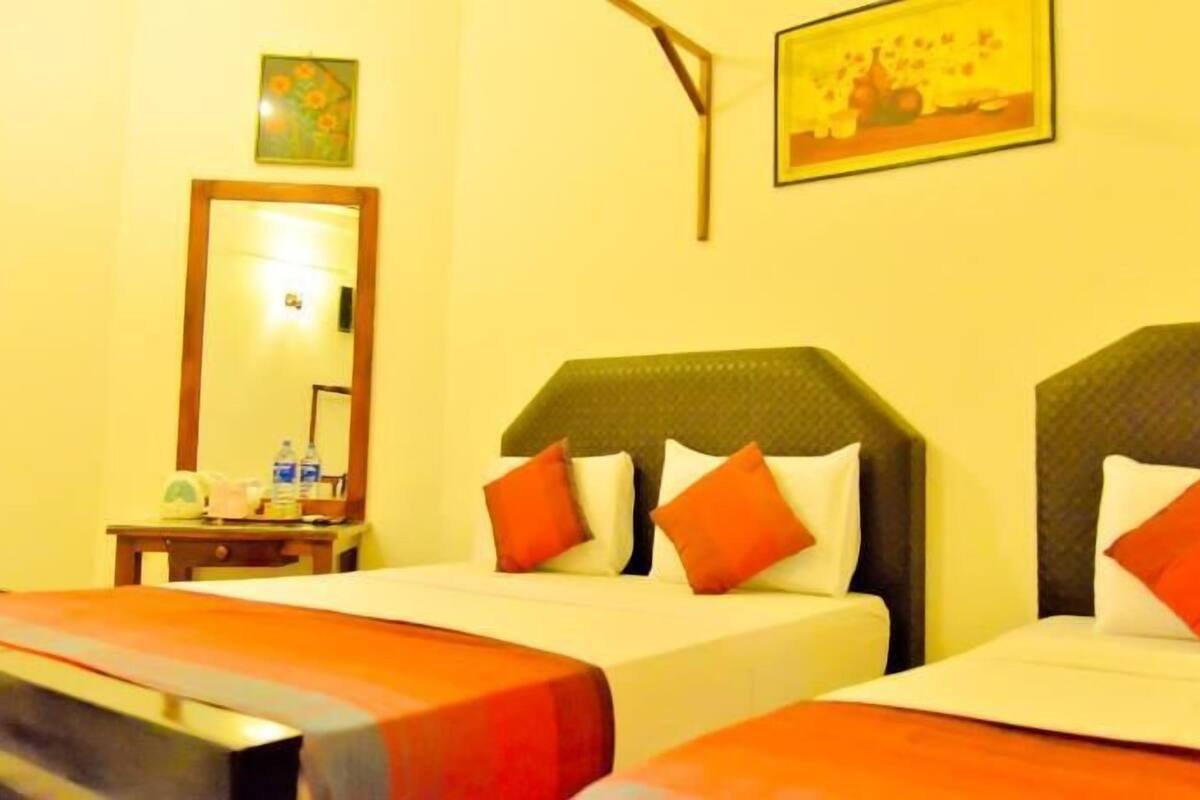 Una habitación de hotel con dos camas, una mesita de noche, un espejo y dos cuadros en la pared.