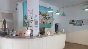 A reception desk with a white counter, a clock, and various informational posters. - Hostal Sunset Ibiza (Sant Antoni de Portmany)