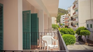 A balcony with white plastic chairs, a green shuttered window, and a view of a narrow street with buildings and greenery. - Hostal Sunset Ibiza (Sant Antoni de Portmany)