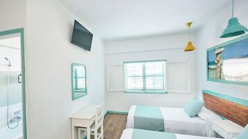 A room with two beds, a desk, a chair, a TV, and a window with shutters.