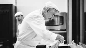 A chef in a white uniform and hat preparing food in a kitchen with stainless steel appliances and a tiled backsplash.