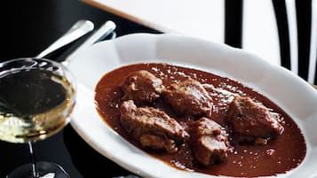 Um prato de ensopado de carne com pães e um copo de vinho branco sobre uma mesa.