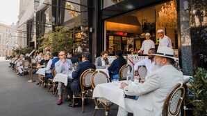 An outdoor café with tables and chairs, a chef in uniform, and a building with a sign. - Hotel Grand Ferdinand Vienna (Vienna)