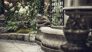 A stone frog statue in a garden with white flowers and a stone fountain. - Hotel Grand Ferdinand Vienna (Vienna)