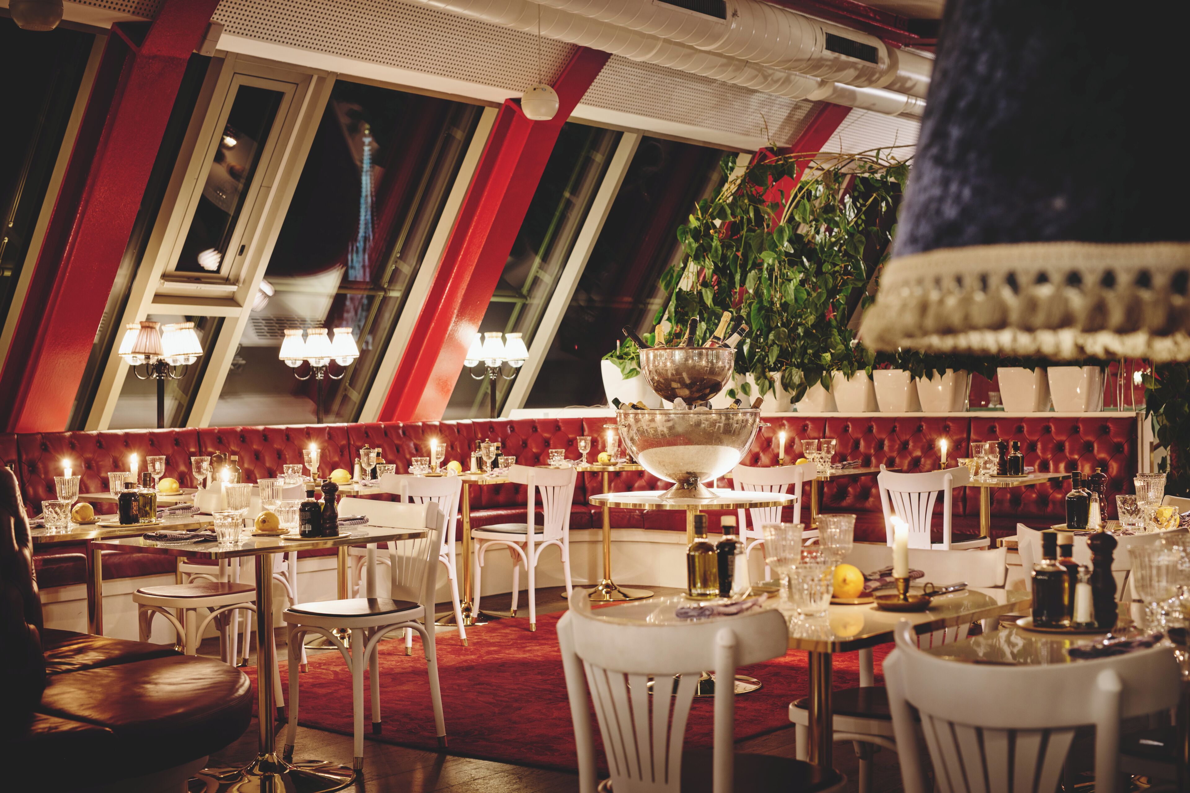 Um restaurante com paredes vermelhas, mobiliário branco e um candelabro.