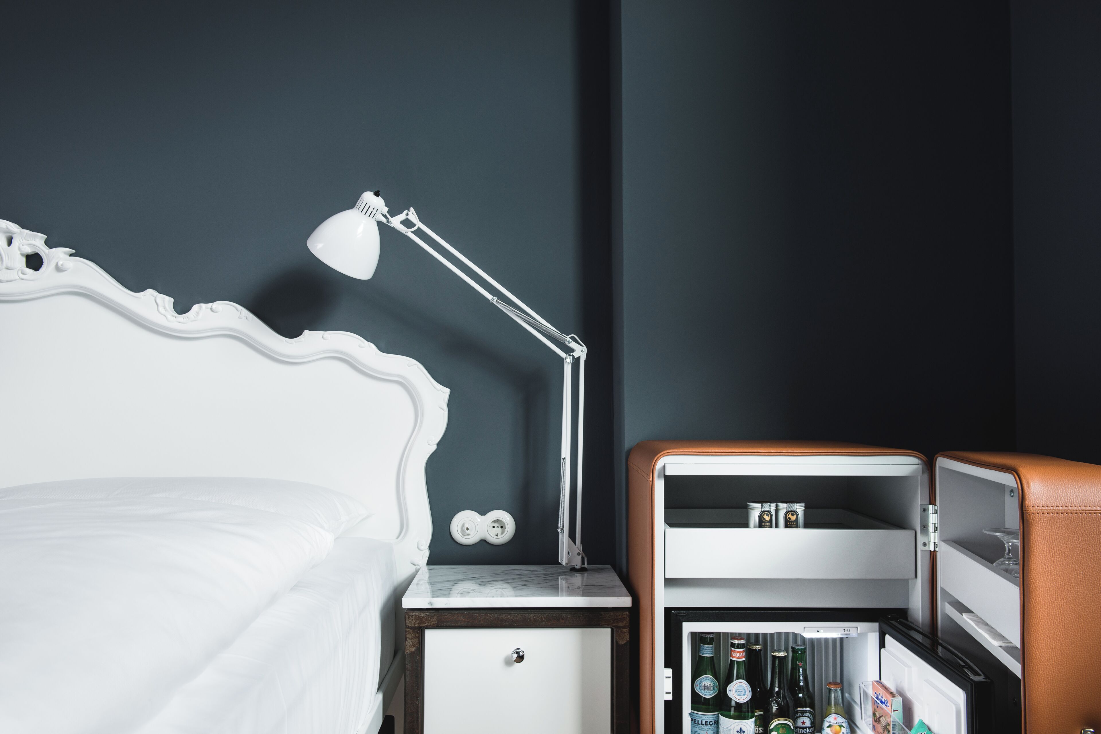 A hotel room with a bed, a nightstand, a desk, and a minibar.