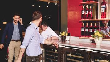 Uma área de bar com um refrigerador de vinho, garrafas de bebidas e um vaso com flores.