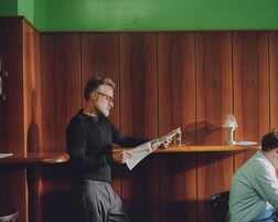 Um homem lendo um menu em um ambiente com painéis de madeira e parede verde.