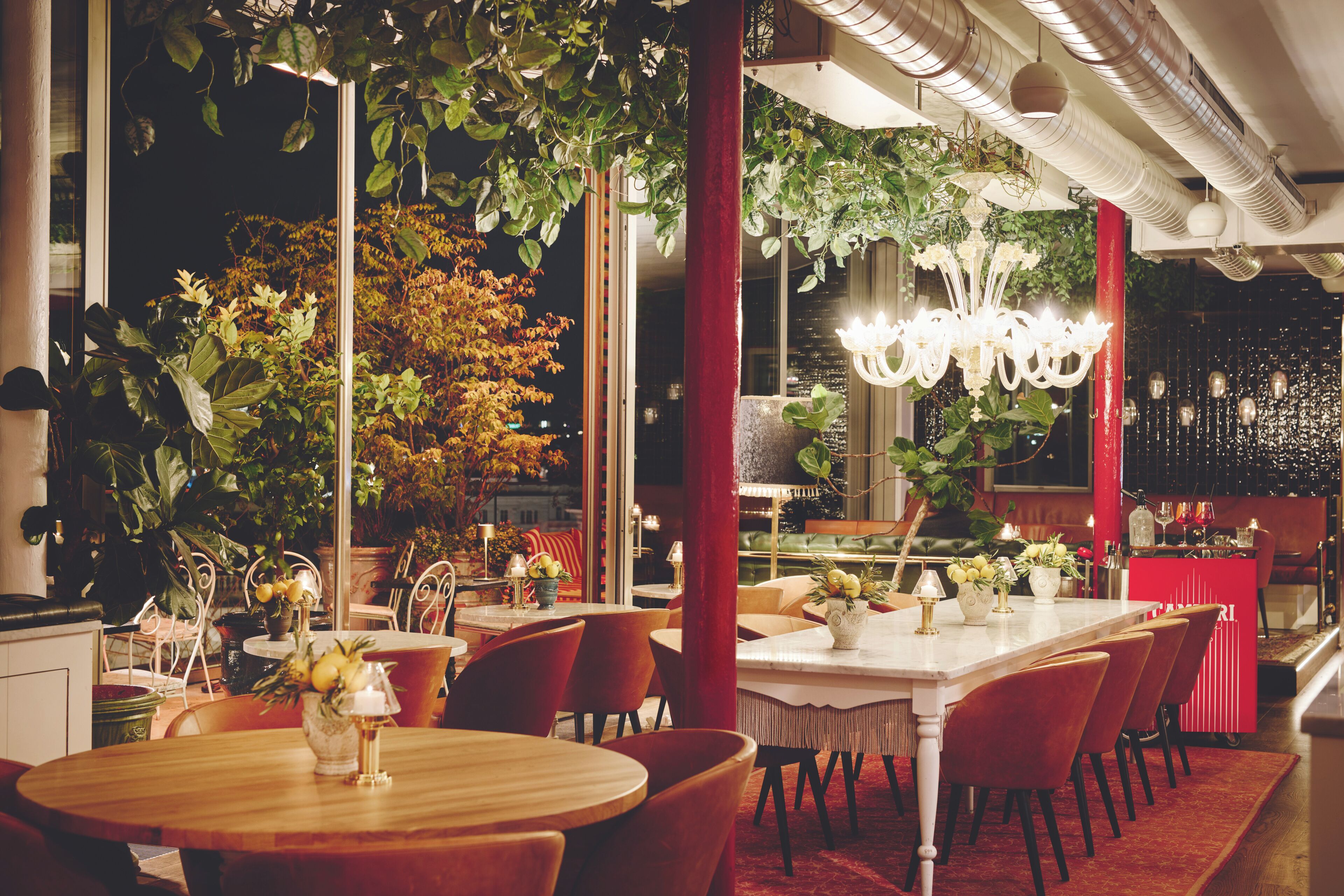 Um restaurante com mesas redondas, cadeiras vermelhas e plantas penduradas.