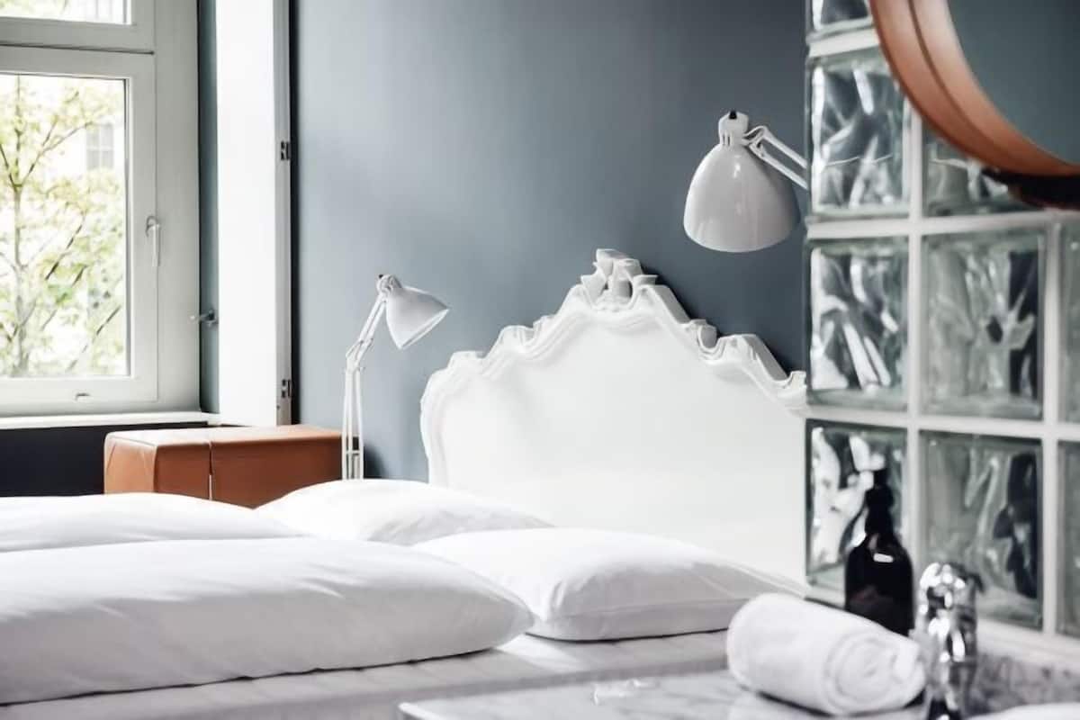 A bedroom with a bed, two bedside lamps, a window, and a mirror.