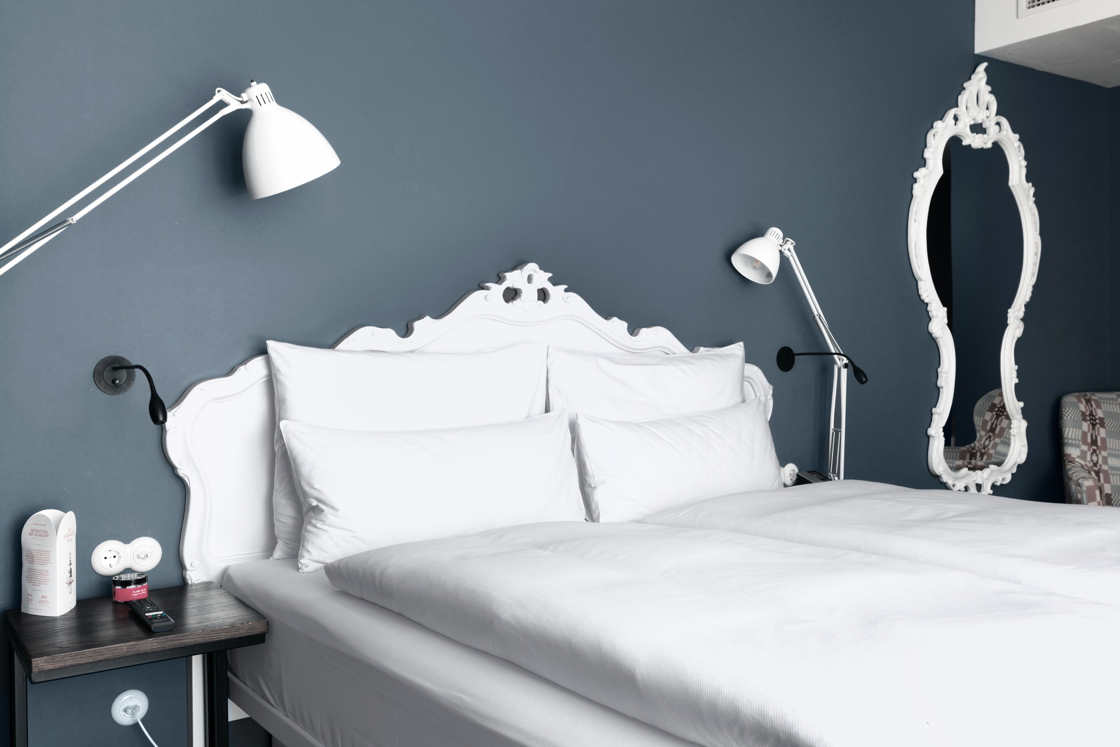 A neatly made bed with white bedding, a white headboard, and two bedside lamps.