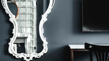A room with a large ornate mirror, a dark wall, a flat-screen TV, and a wooden chair.