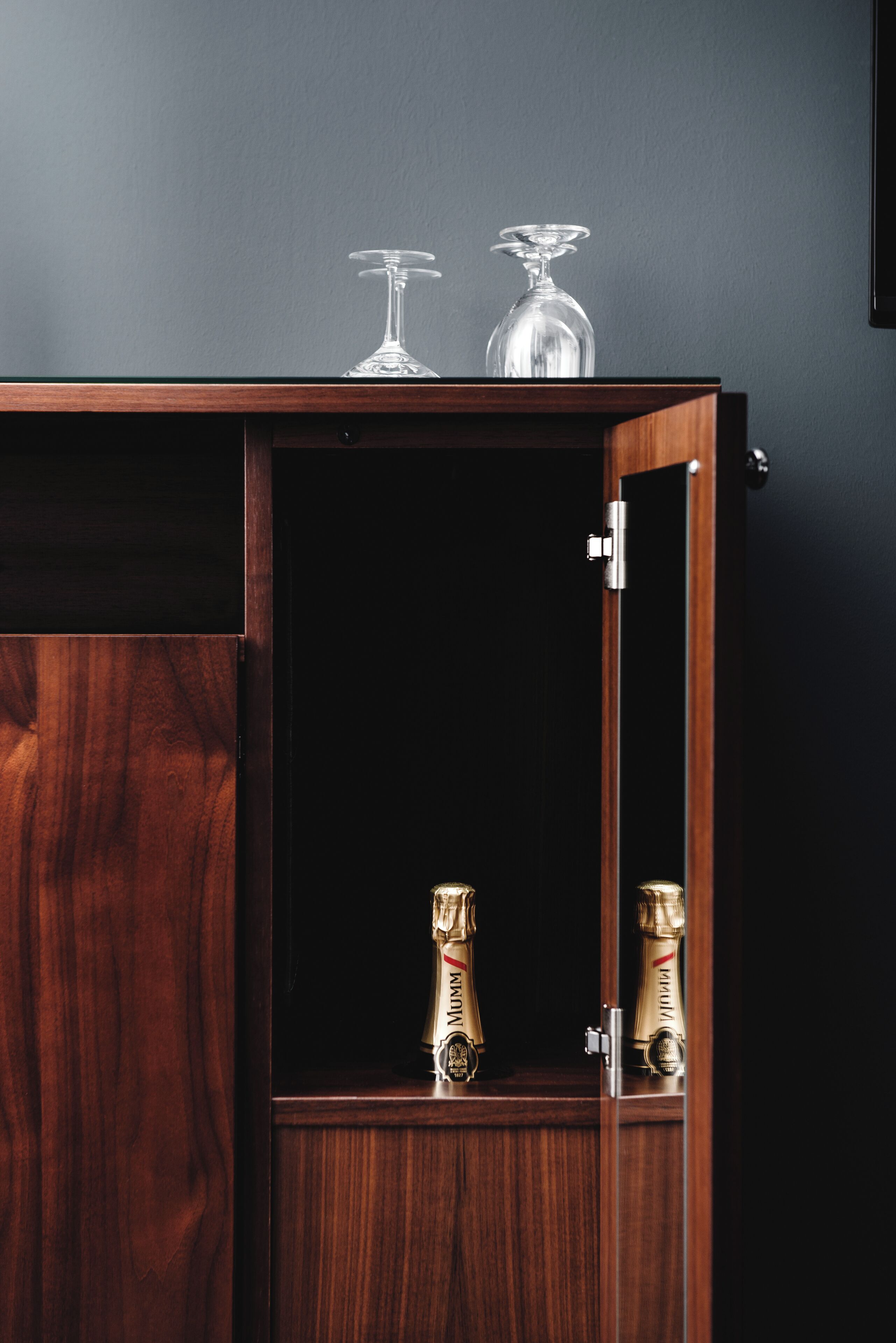 A wooden cabinet with a dark interior, two champagne flutes, and a clear glass on top.