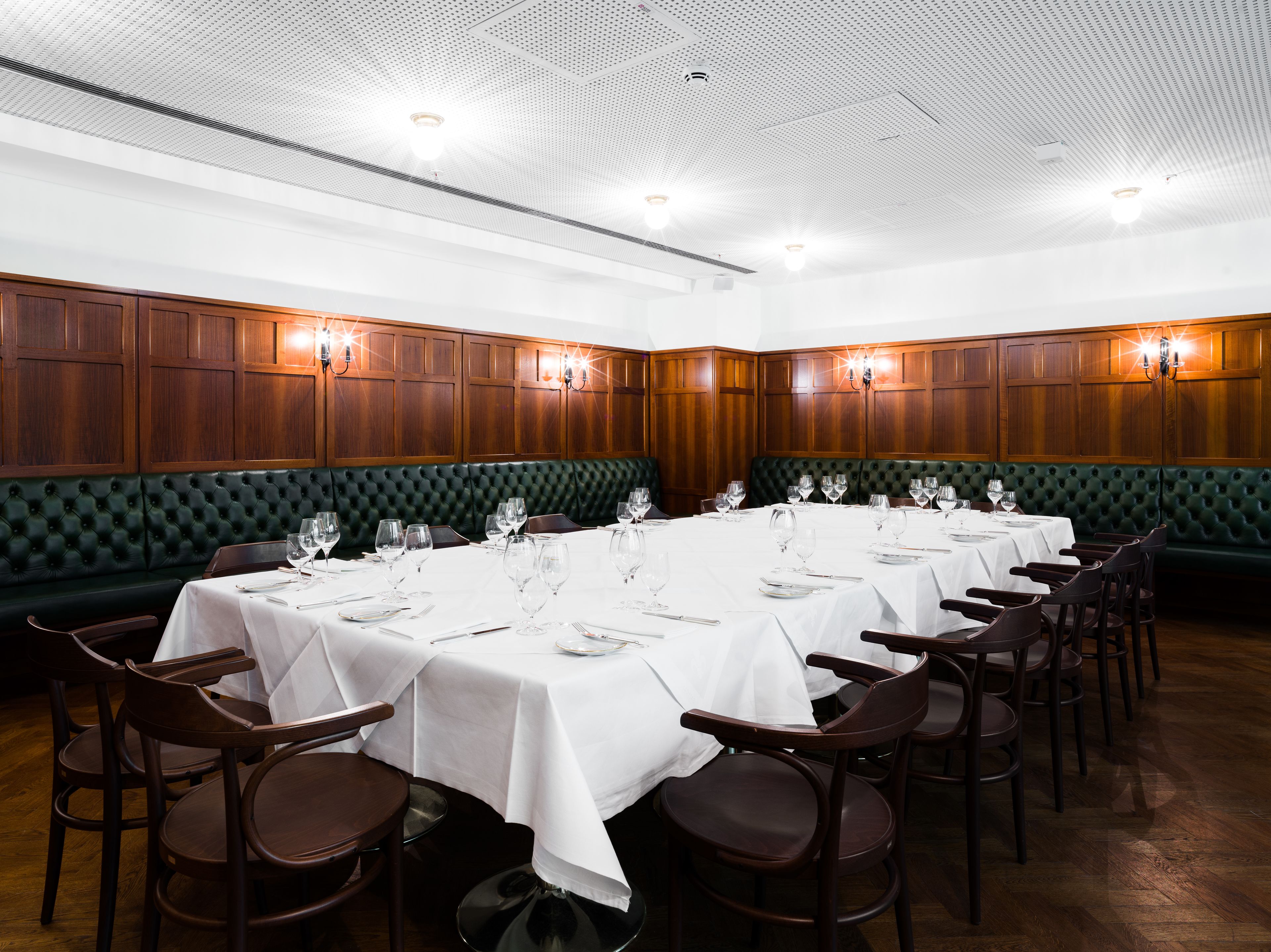 Un comedor formal con varias mesas dispuestas para el servicio, cabinas tapizadas en verde y paneles de madera en las paredes.