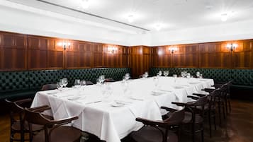 Un comedor formal con varias mesas dispuestas para el servicio, cabinas tapizadas en verde y paneles de madera en las paredes.