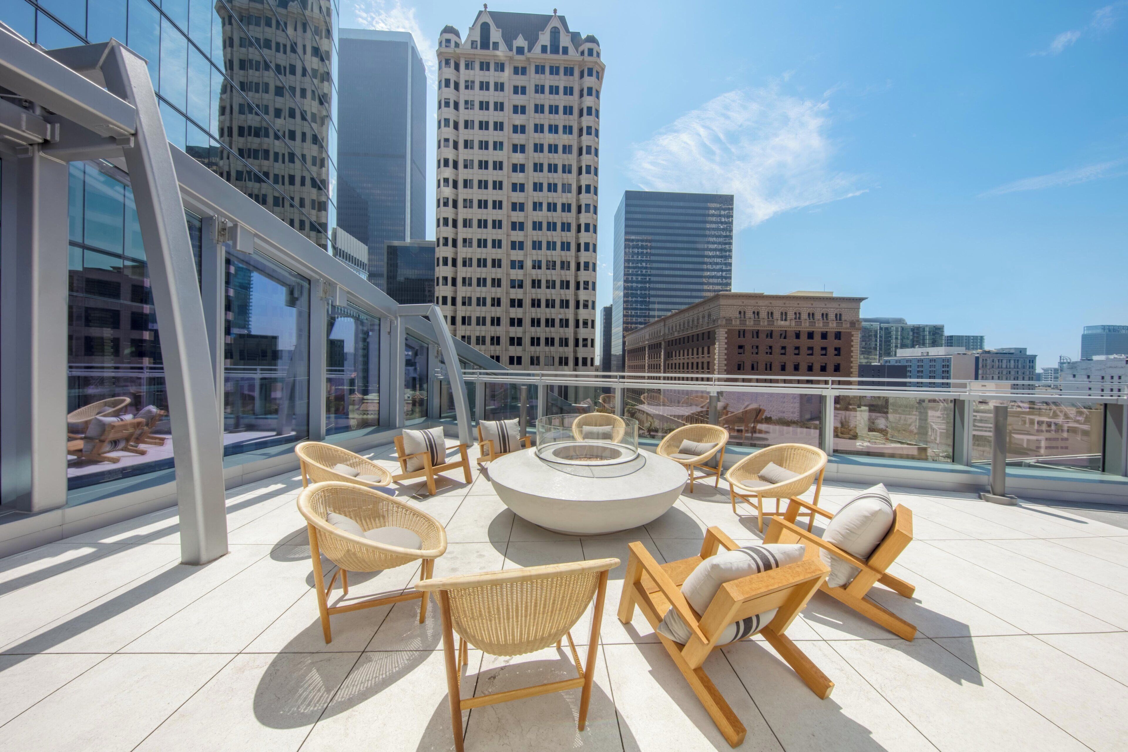 Una terrazza sul tetto con un tavolo rotondo e sedie in vimini, con vista su un paesaggio urbano caratterizzato da edifici moderni.