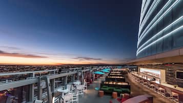 A rooftop bar with outdoor seating, a city view, and a modern building facade.