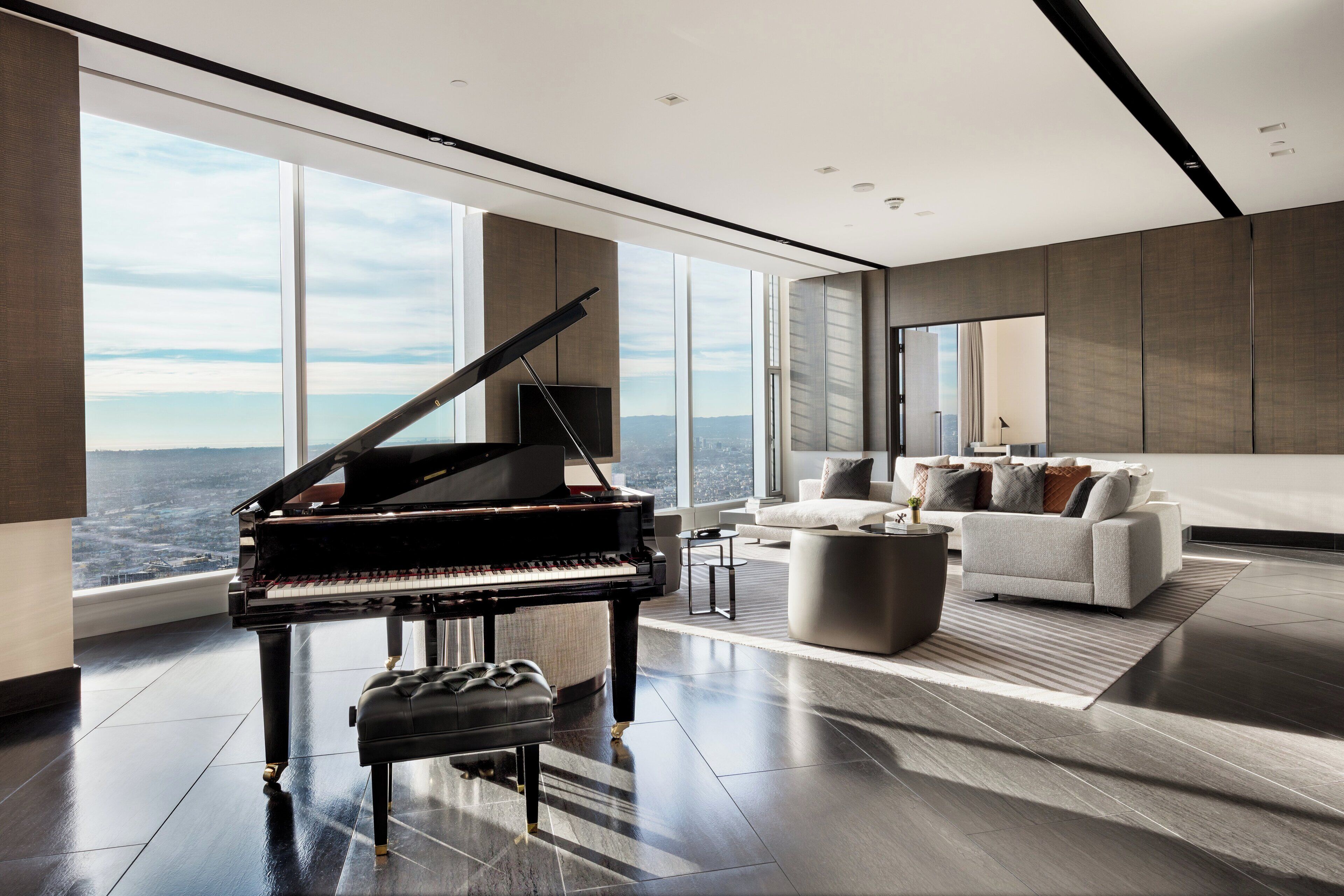 Un salon spacieux avec un grand piano, un canapé moderne et une vue sur la ville grâce à de grandes fenêtres.