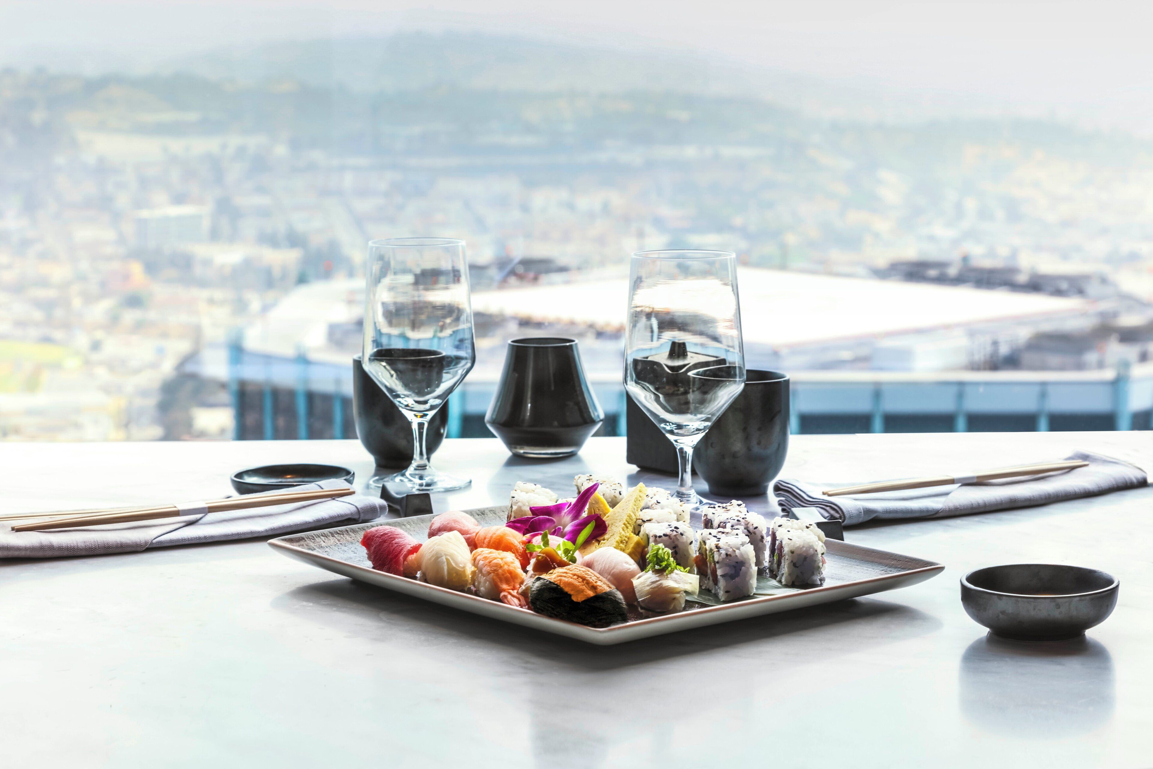 Une table avec un plateau de sushis, deux verres d’eau, des baguettes, un bol et une vue sur un stade.