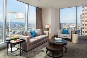 Ein modernes Hotelzimmer mit weiter Aussicht auf die Stadt, einem Sofa, einem Sessel, einem kleinen Tisch und einer Lampe.