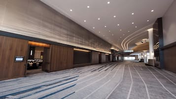 A spacious hotel lobby with a modern design, featuring a large carpeted area, a reception desk, and a sign indicating the location of the grand ballroom.