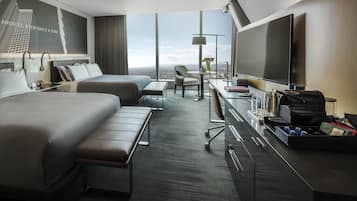 Una habitación de hotel moderna con una cama grande, un escritorio con televisor, una silla y vista a la ciudad.