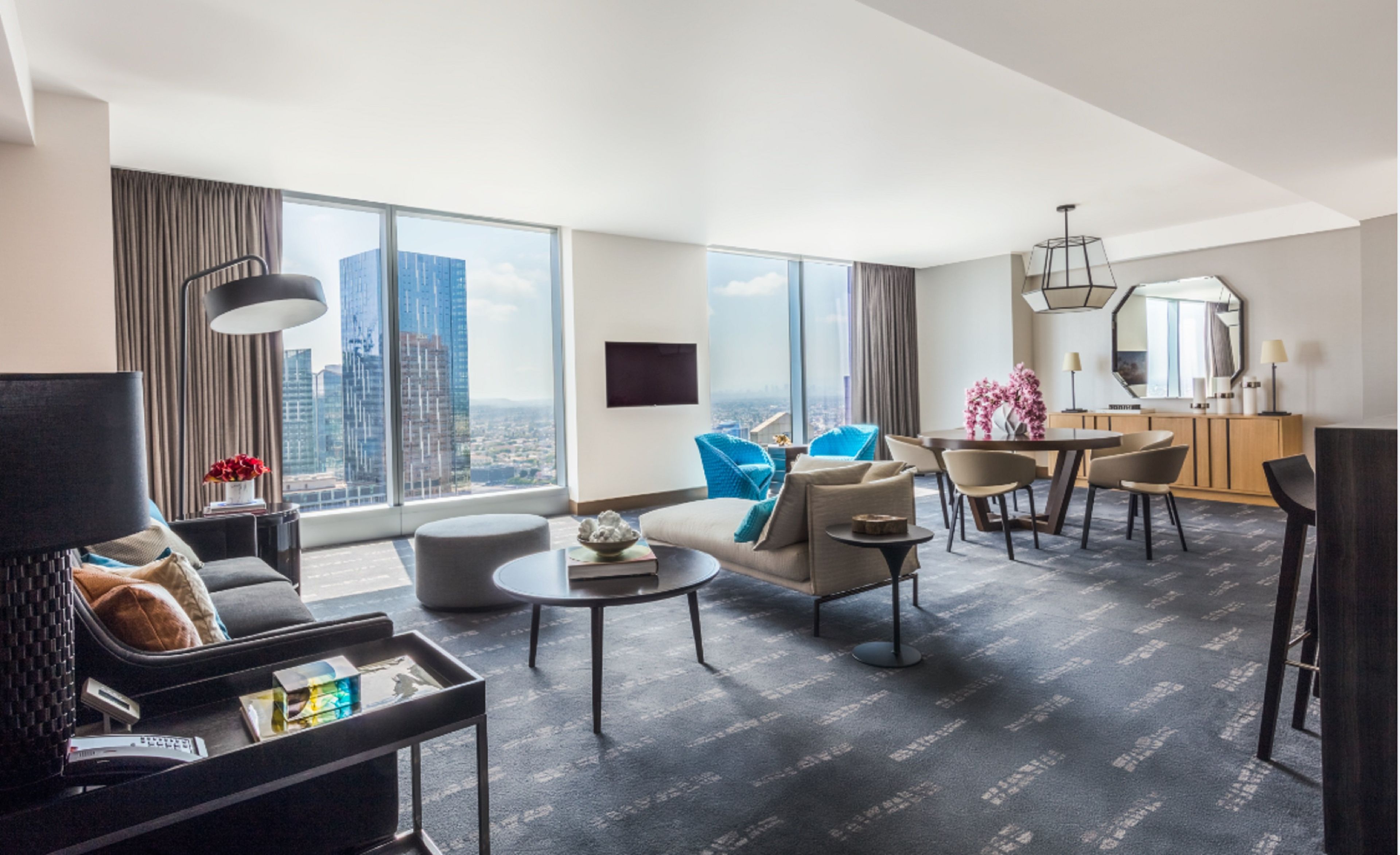 Et moderne hotelværelse med udsigt over byen, et spiseområde og en siddeplads med sofa og stole.