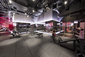 Ein modernes Fitnessstudio mit verschiedenen Trainingsgeräten, darunter Kurzhanteln, Bänke und Kraftgeräte.