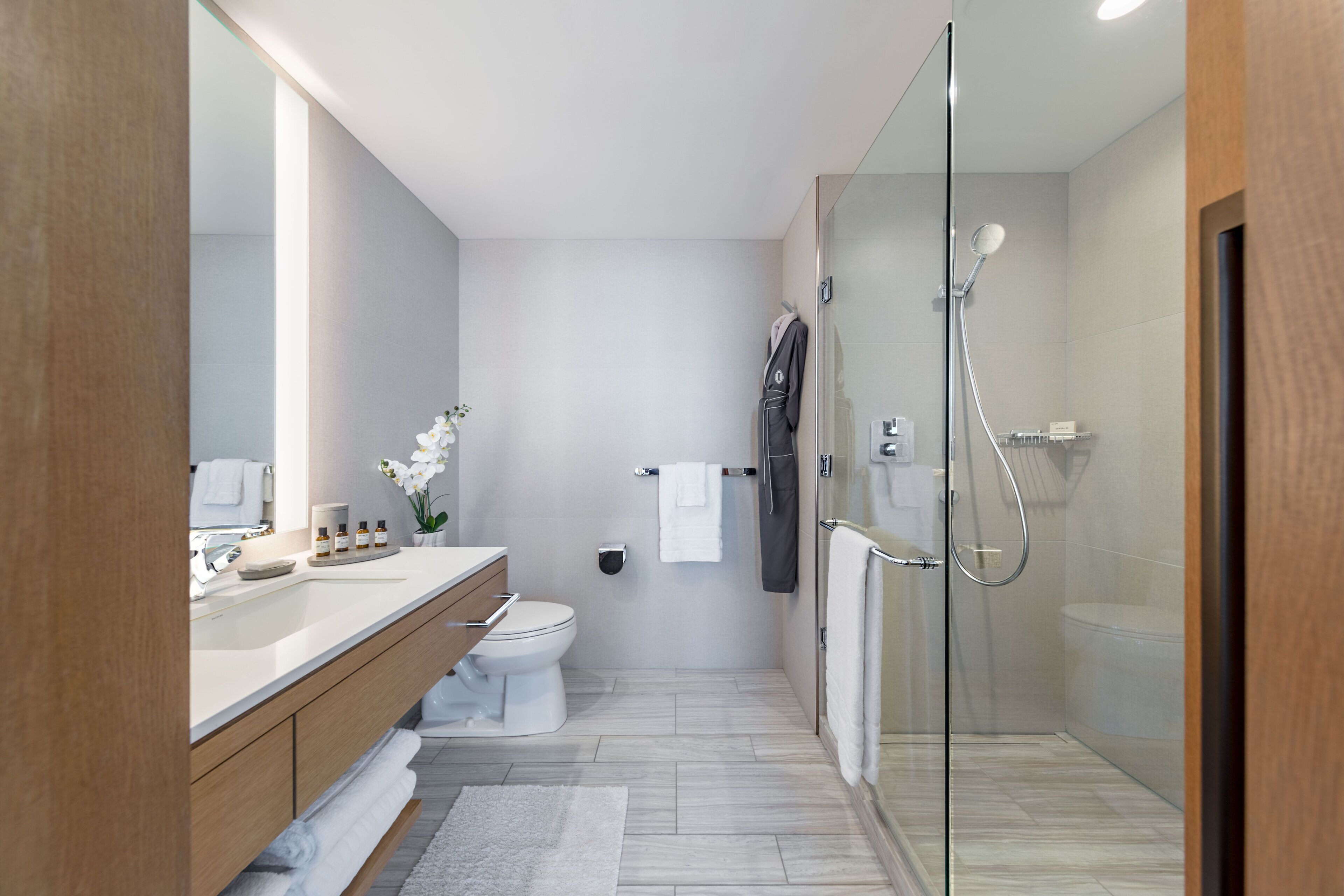 Un baño moderno con cabina de ducha de vidrio, tocador de madera, inodoro blanco y un espejo grande.
