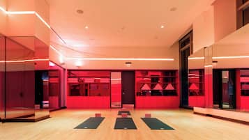 A spacious room with a wooden floor, red lighting, and a mirrored wall.