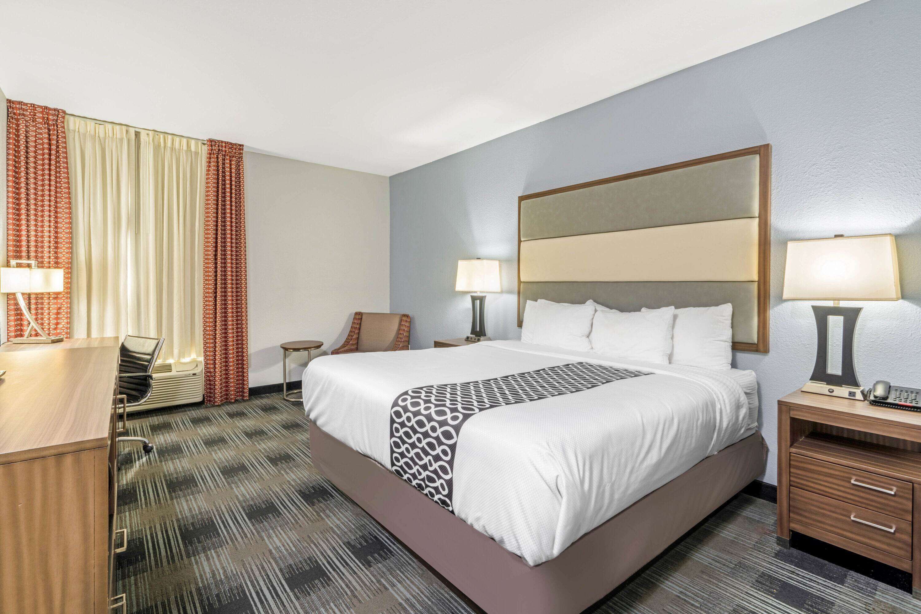A hotel room with a large bed, two bedside tables with lamps, a desk, and a chair.