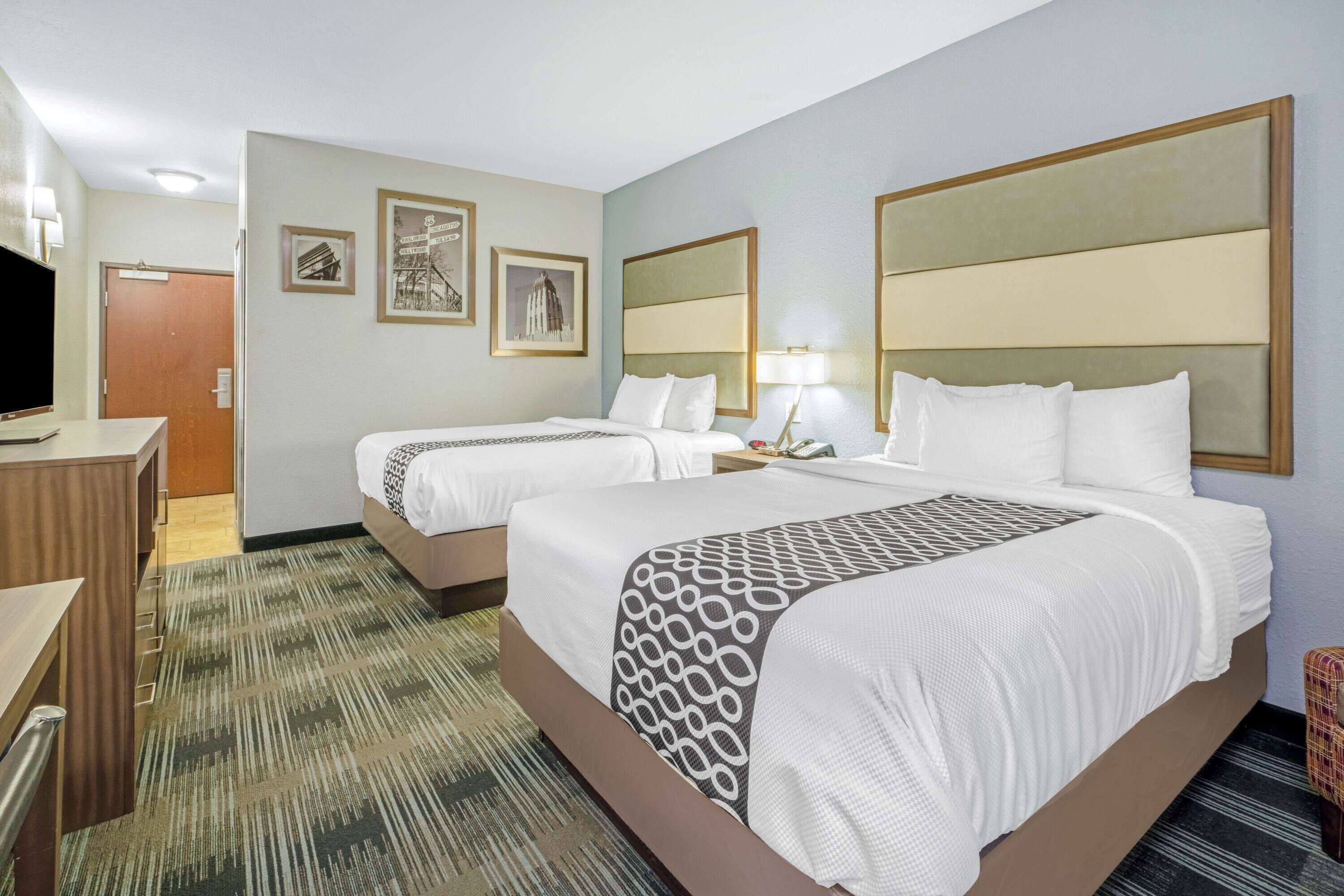 A hotel room with two beds, a desk, a TV, and a carpeted floor.