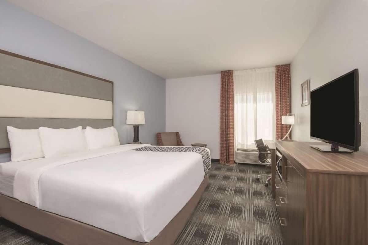 A hotel room with a large bed, a desk with a television, a chair, and a window with curtains.