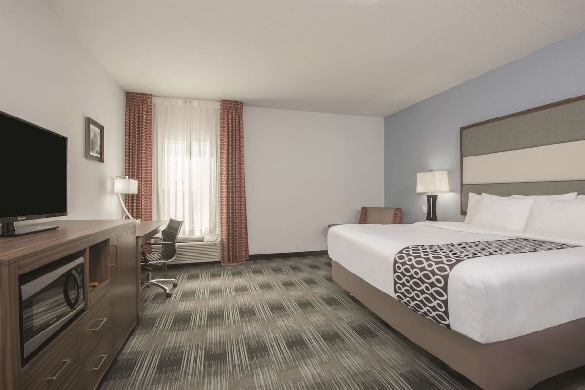 A hotel room with a bed, a desk with a computer, a TV, and a window with curtains.