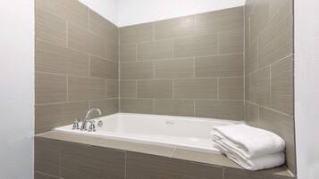 Een moderne badkamer met een vrijstaand bad, een wastafel met een kraan en een stapel witte handdoeken.