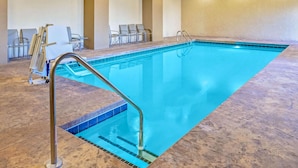 An indoor swimming pool with a clear blue water, a metal ladder, and several empty lounge chairs against the wall.