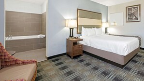 A hotel room with a bed, nightstands, a sofa, a bathroom with a bathtub, and a wall-mounted picture.