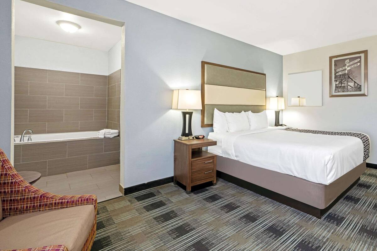 A hotel room with a bed, nightstands, a sofa, a bathroom with a bathtub, and a wall-mounted picture.