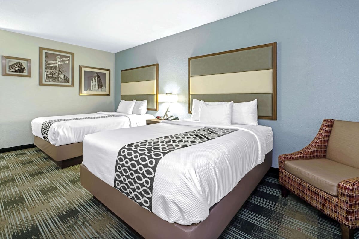 A hotel room with two beds, a chair, and framed pictures on the wall.