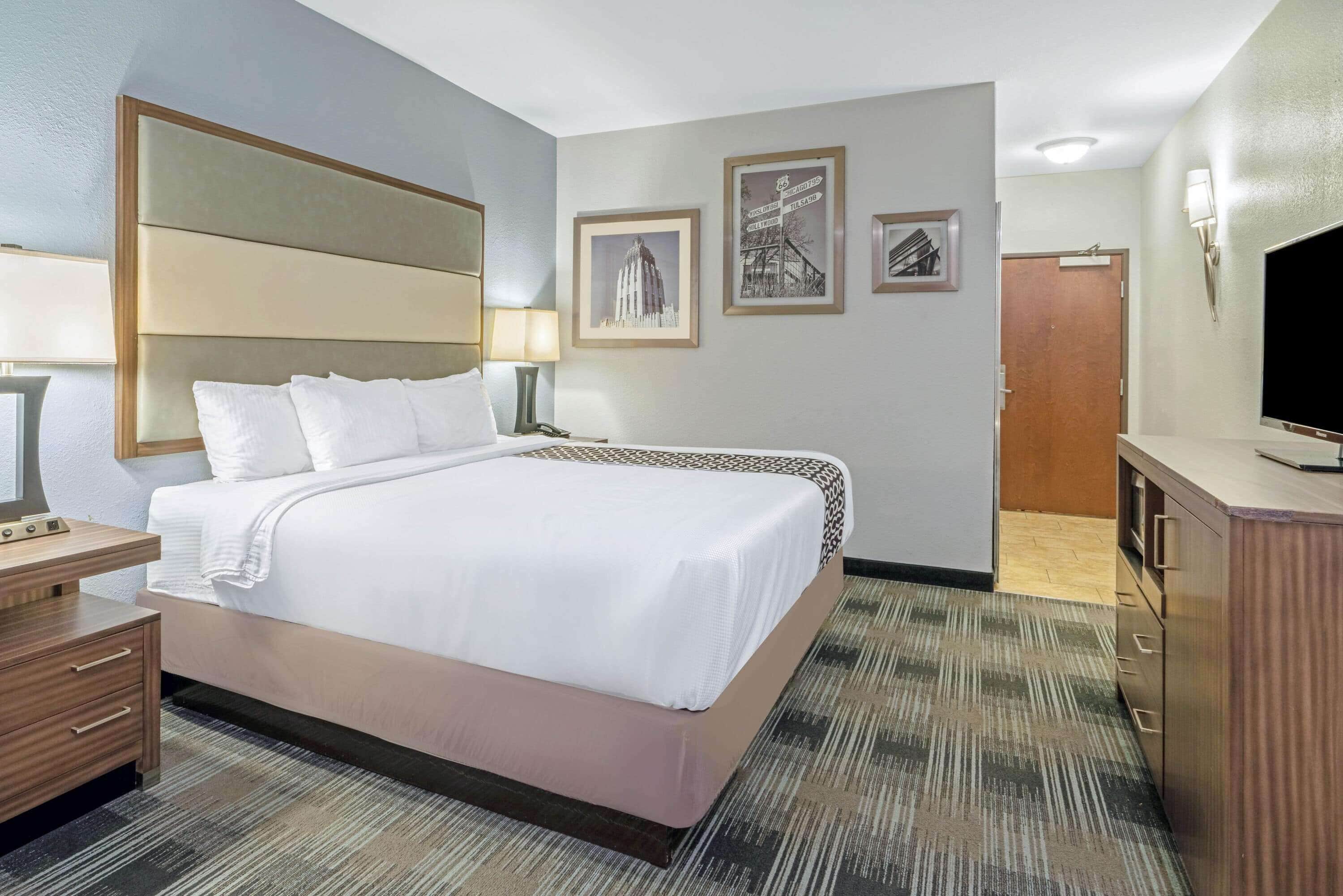 A hotel room with a large bed, bedside tables, a desk, a television, and framed pictures on the wall.